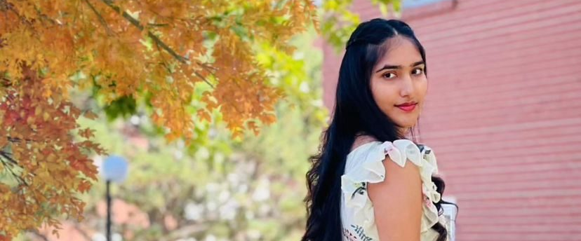 Woman standing outdoors with autumn foliage and a pink building in the background